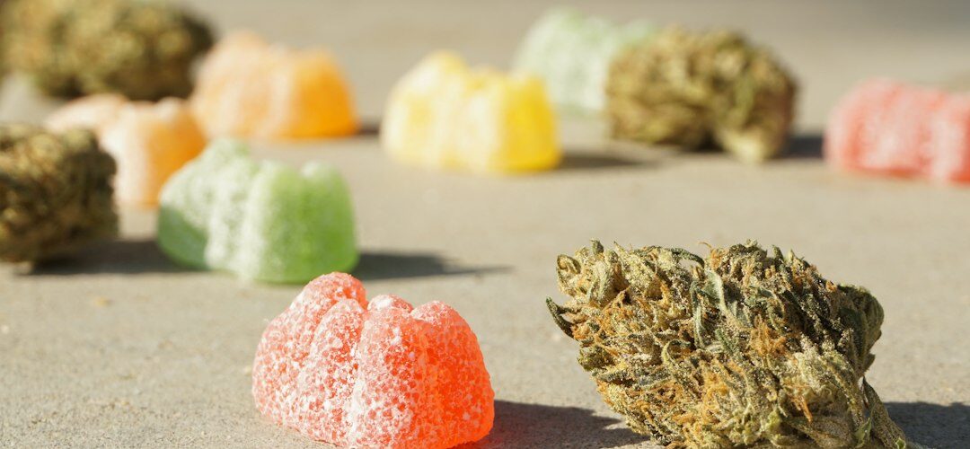 Colorful gummies and cannabis bud on surface